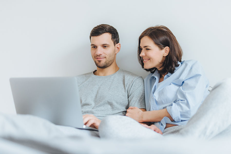 Liebevoll Frau und Mann haben gemeinsam Freude, schauen Film im Schlafzimmer auf Laptop